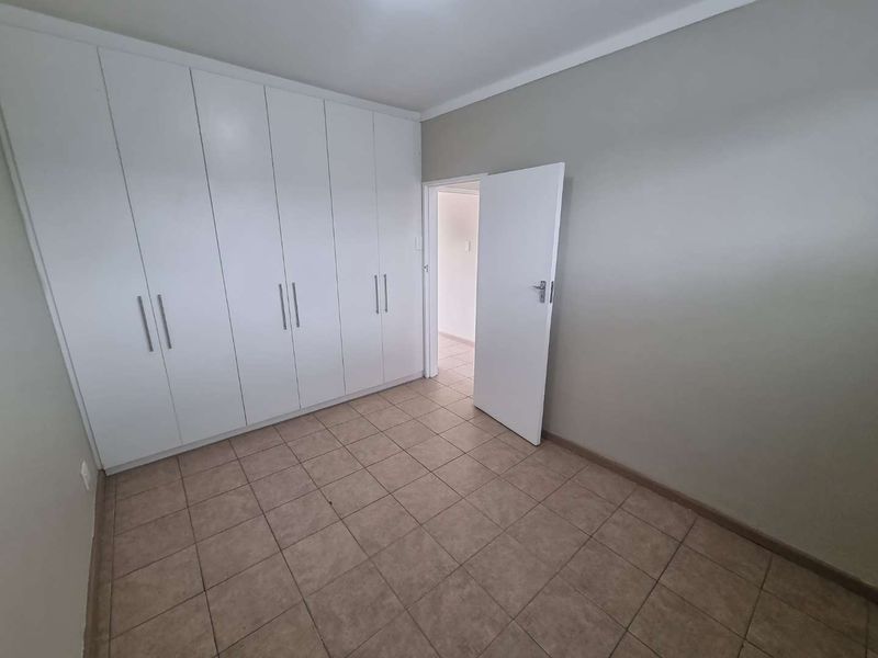A clean, empty bedroom featuring neutral wall tones, tiled flooring, and ample built-in cupboard storage space.