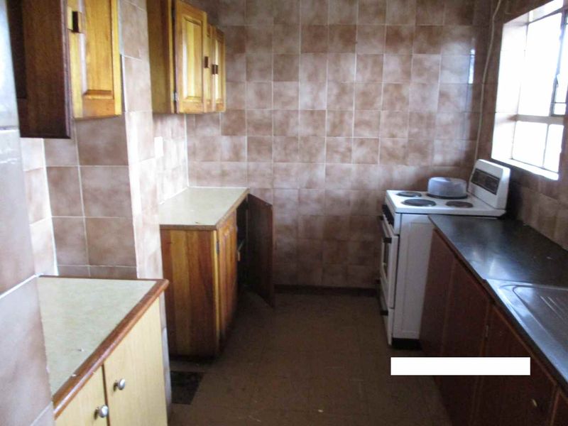 A dated kitchen featuring wooden cabinetry, tiled wall splashbacks, and a freestanding stove, offering potential for a modern renovation.