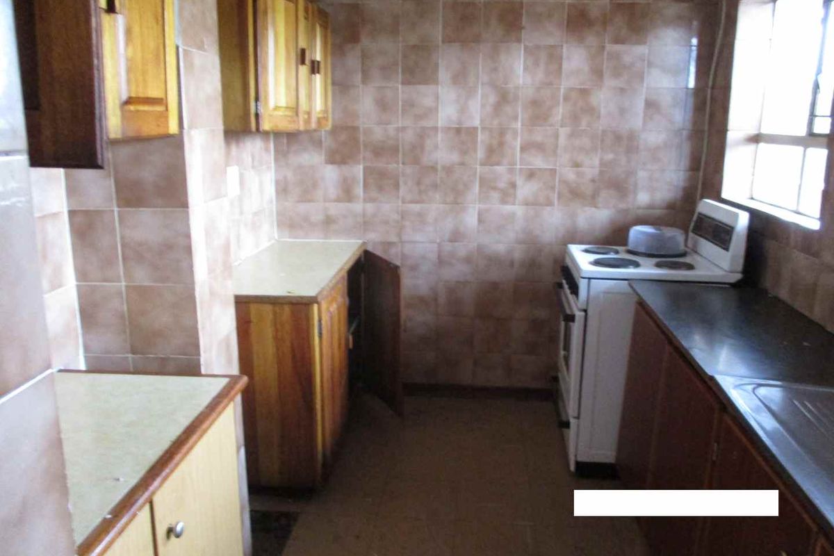 A dated kitchen featuring wooden cabinetry, tiled wall splashbacks, and a freestanding stove, offering potential for a modern renovation.