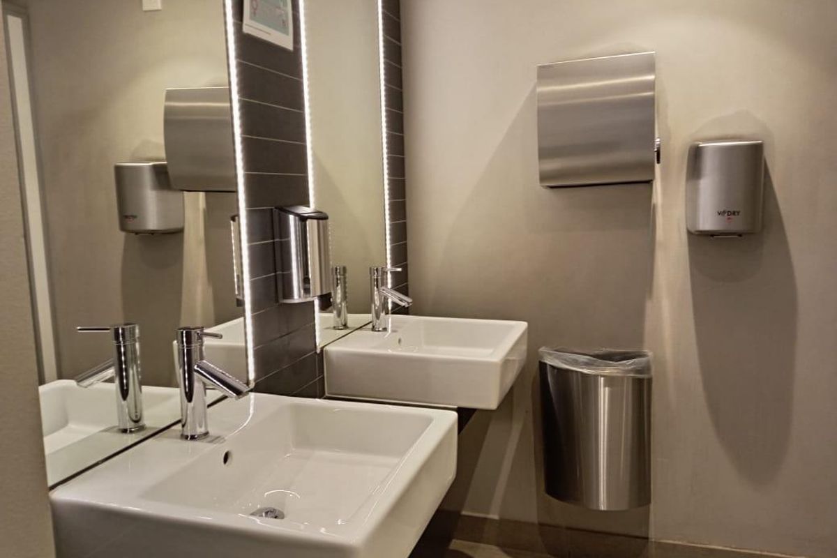 Modern office restroom featuring dual wall-mounted washbasins, chrome fixtures, integrated LED mirror lighting, and professional stainless steel accessories.