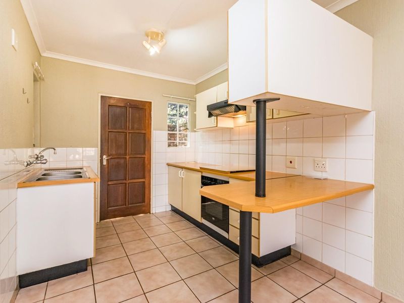 A functional kitchen featuring built-in cabinetry, laminate countertops, a breakfast bar, and integrated oven with extractor fan, finished with ceramic tile flooring.