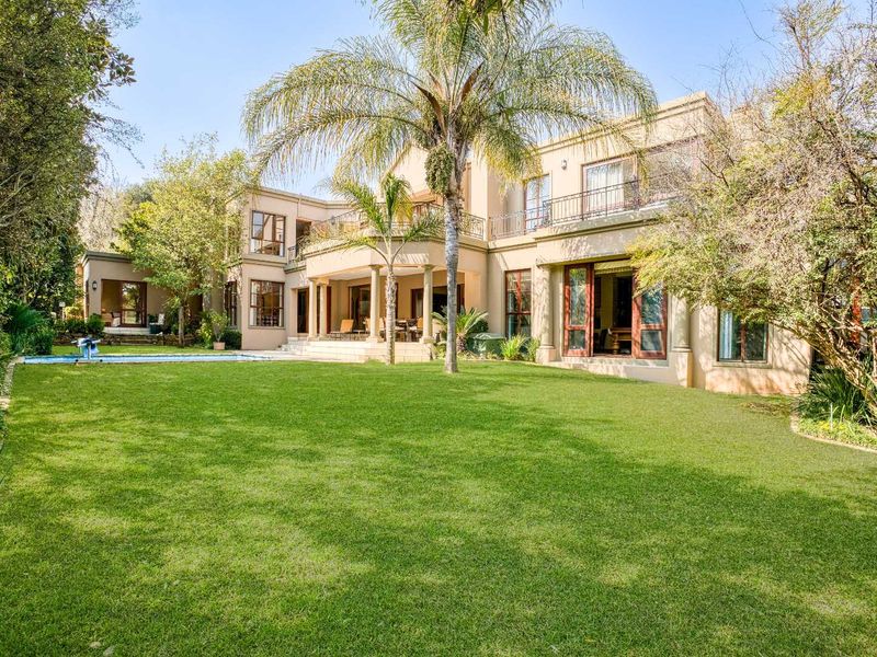 Spacious rear garden featuring a well-maintained lawn, swimming pool, and a large covered patio with balcony access above.