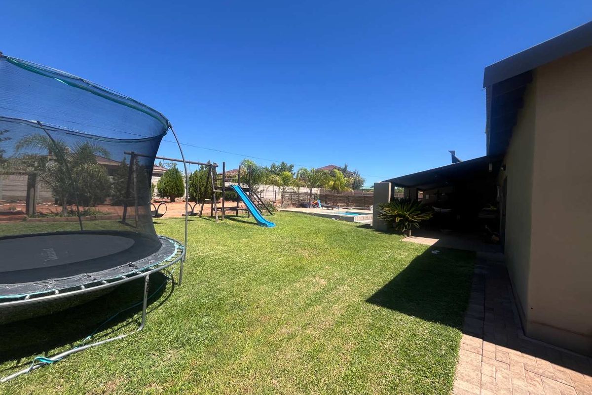 Spacious rear garden featuring a lawn, a covered patio area, and a swimming pool, providing an ideal space for outdoor recreation and entertainment.