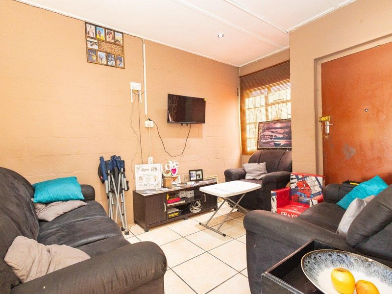 A compact living room featuring tiled flooring, recessed lighting, and a security gate, offering a functional space ready for cosmetic updates.