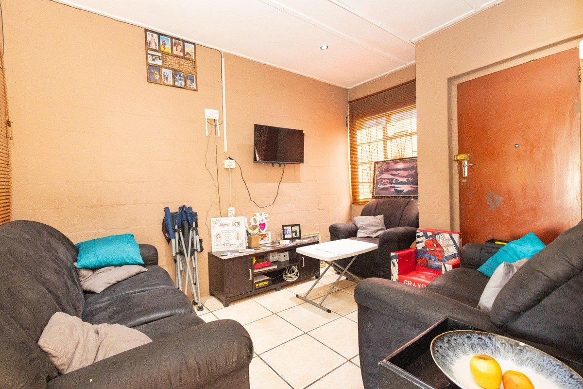 A compact living room featuring tiled flooring, recessed lighting, and a security gate, offering a functional space ready for cosmetic updates.