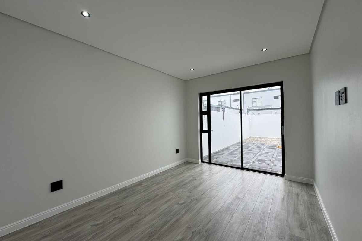A bright, modern bedroom featuring neutral finishes, recessed ceiling lighting, and large sliding glass doors that open onto a private paved patio area.