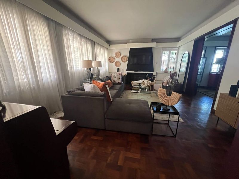 Spacious living room featuring classic parquet flooring, a central fireplace, and large windows with sheer curtains, offering a warm and inviting atmosphere.