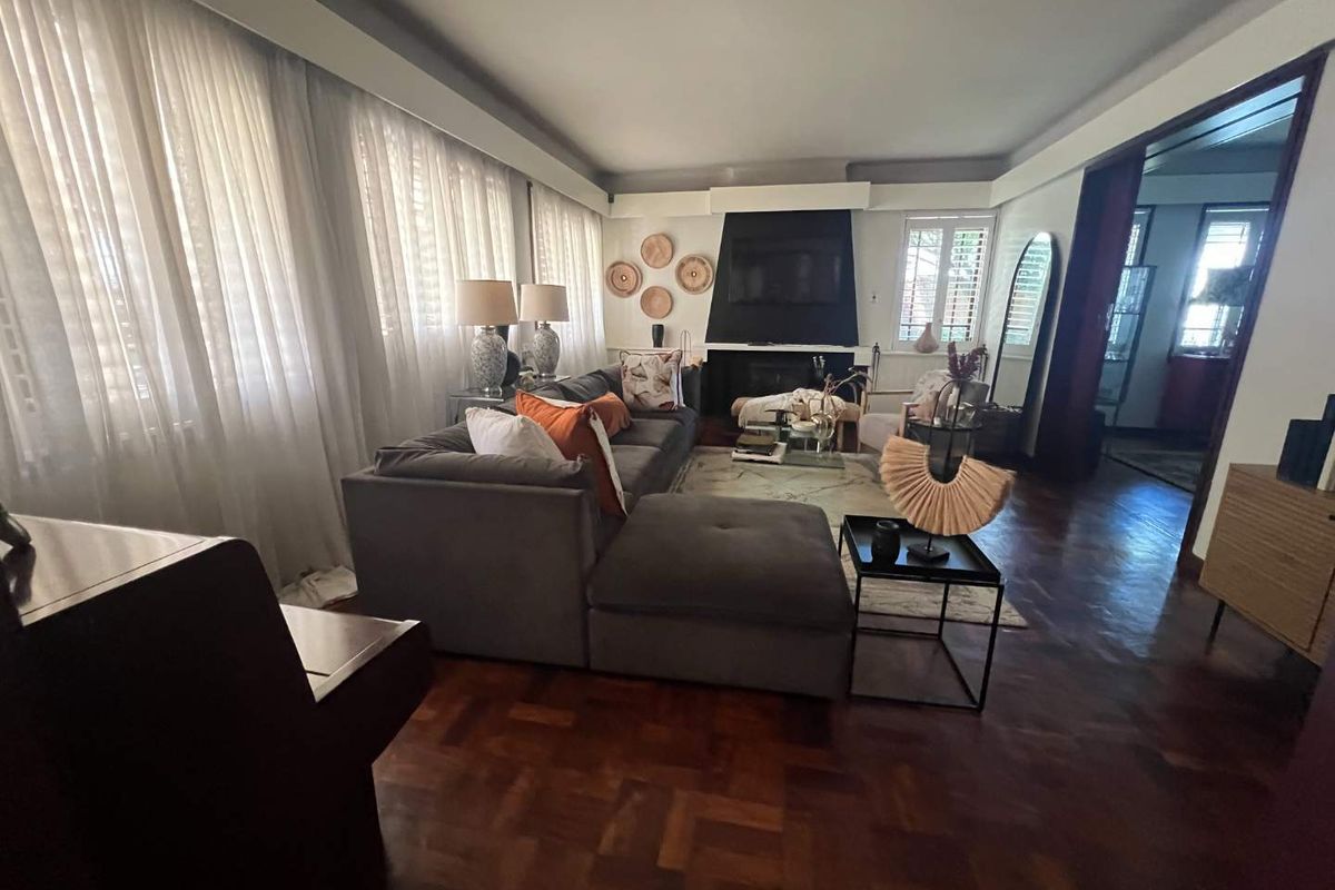 Spacious living room featuring classic parquet flooring, a central fireplace, and large windows with sheer curtains, offering a warm and inviting atmosphere.