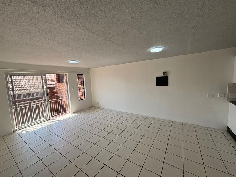An empty open-plan living area featuring tiled flooring, ceiling lights, and a sliding glass door leading to a balcony with security gate.