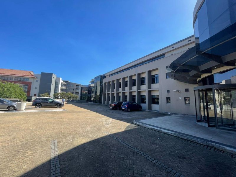 Exterior view of a modern office building featuring a paved parking area, glass facade, and a prominent revolving entrance door.
