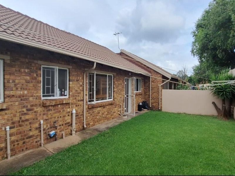 Rear view of the townhouse featuring a face brick exterior, tiled roof, and a private grassed garden area with boundary walling.