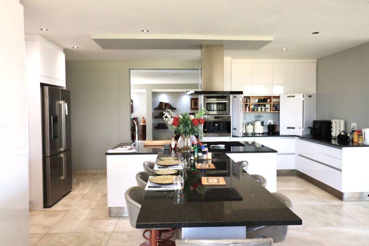 Modern open-plan kitchen featuring high-gloss cabinetry, a large central island with a breakfast bar, integrated appliances, and sleek stone countertops.
