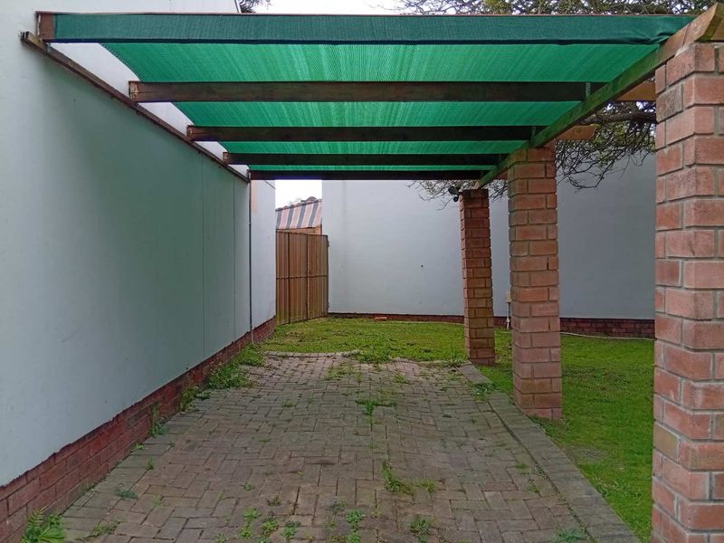 A covered outdoor patio area featuring brick pillars, a timber pergola frame with shade cloth, and paved flooring, set within a private garden space.
