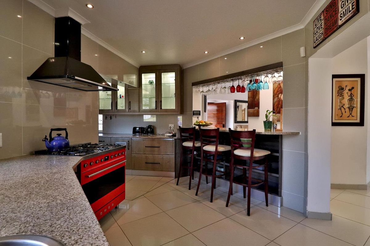 Modern kitchen featuring granite countertops, built-in cabinetry, a prominent red Smeg gas range with extractor hood, and a breakfast bar with overhead glass storage.