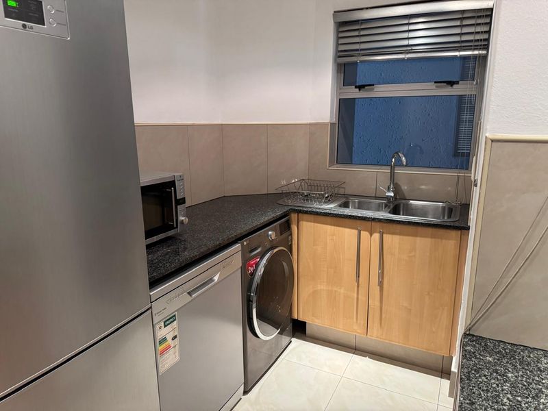 A functional scullery area featuring granite countertops, wooden cabinetry, a double sink with mixer tap, and tiled backsplash.