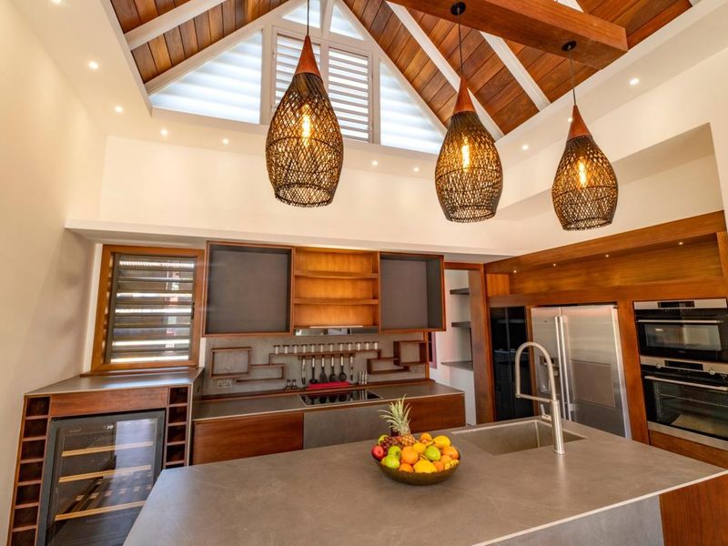 Modern kitchen featuring high vaulted timber ceilings, custom wood cabinetry, integrated appliances, a central island with sink, and stylish pendant lighting.
