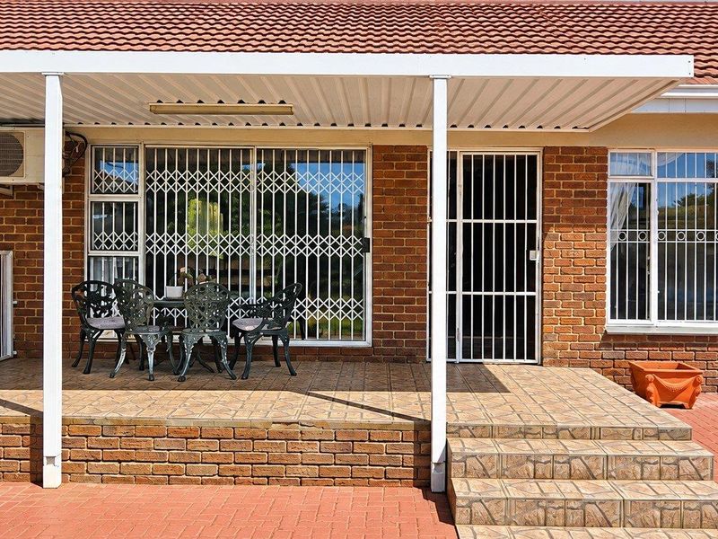 A covered brick patio area featuring tiled flooring, security gates, and exterior security bars, providing a functional outdoor space for relaxation.