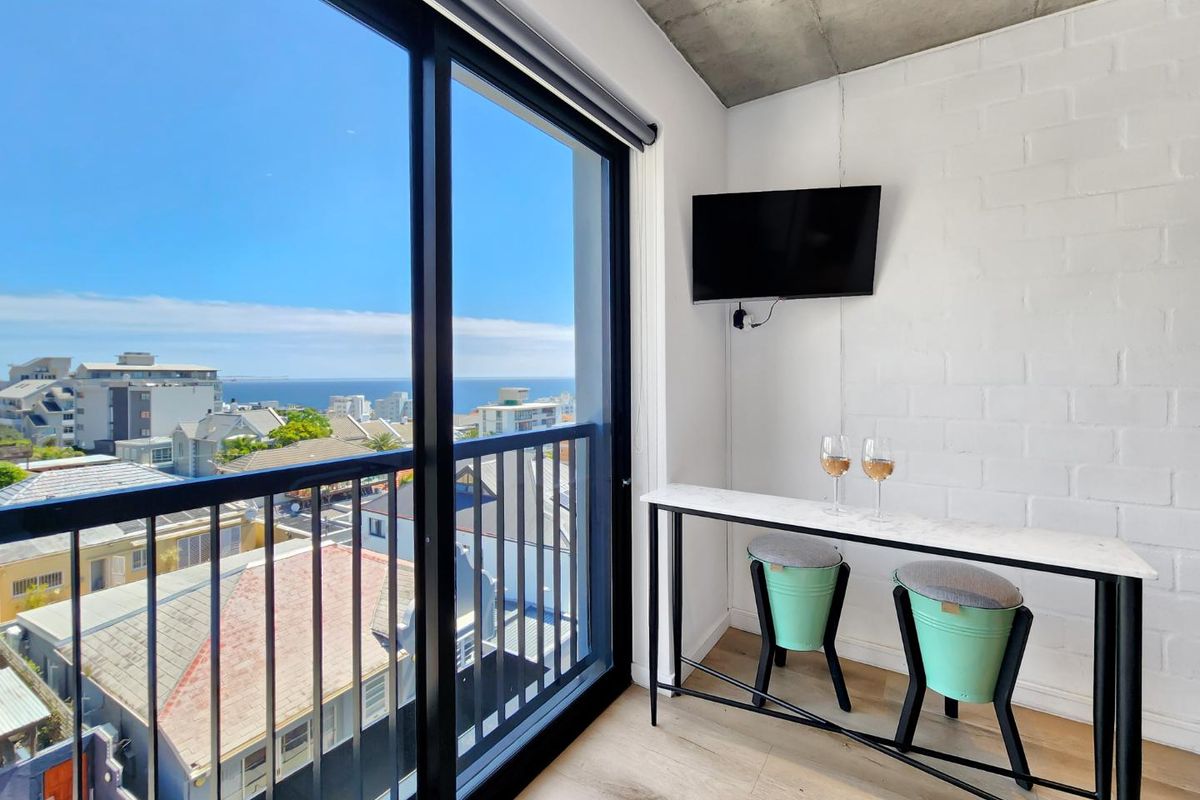 Modern living area featuring exposed concrete ceilings, painted brick walls, and large sliding glass doors opening to a balcony with coastal views.