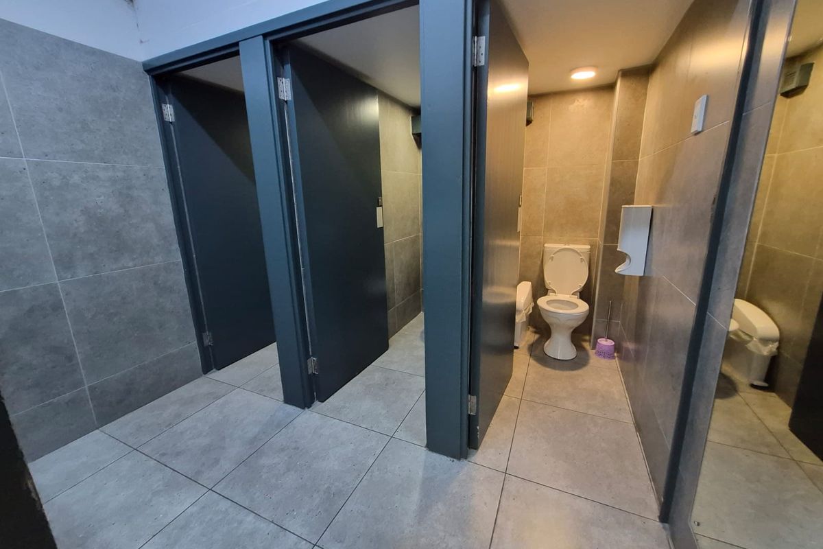 A clean, modern office bathroom featuring multiple private toilet cubicles with grey tiled walls and flooring and recessed lighting.