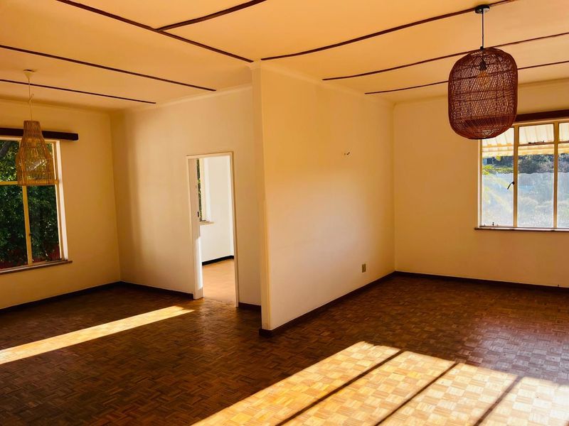 Spacious, light-filled living area featuring classic parquet flooring and distinctive timber ceiling beams, offering a versatile blank canvas for interior design.