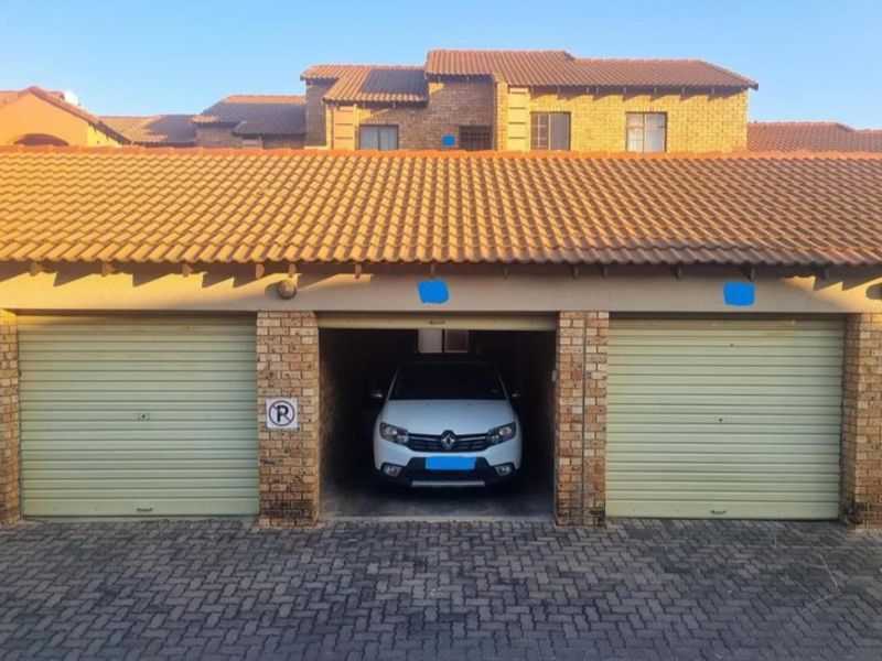 A multi-bay garage structure featuring brick pillars, roll-up doors, and a tiled roof, situated in a residential apartment complex.