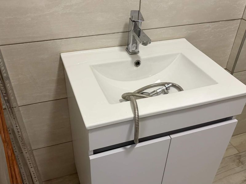 A modern bathroom vanity unit featuring a white cabinet, ceramic basin, and chrome mixer tap, set against neutral wall tiles.