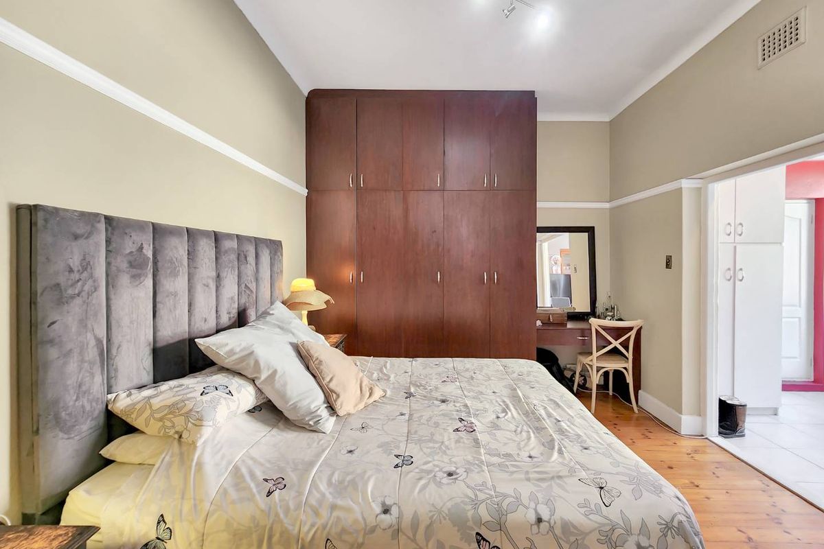 A well-maintained bedroom featuring warm timber flooring, classic picture rails, and extensive floor-to-ceiling built-in wooden cabinetry.
