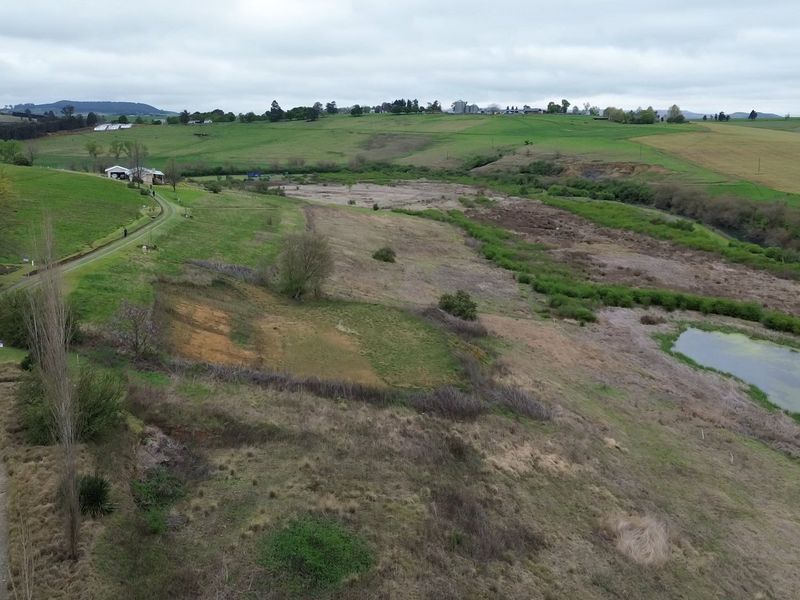 Aerial view of a large, undeveloped residential land parcel featuring natural terrain, a small pond, and an existing gravel access road.