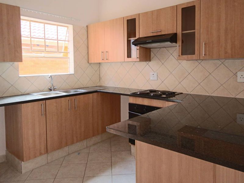 A functional kitchen featuring light wood-finish cabinetry, dark granite countertops, a built-in oven with gas hob, and a tiled backsplash.