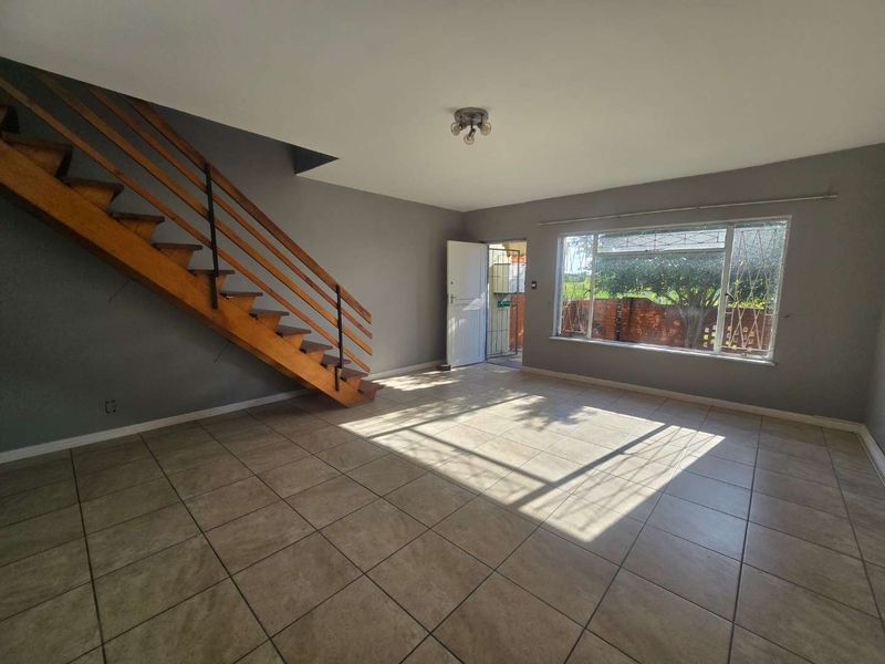 Spacious open-plan living area featuring tiled flooring, a prominent wooden staircase, and large windows providing natural light and garden views.