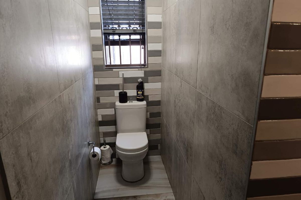 A compact, modern bathroom featuring floor-to-ceiling grey tiled walls, a contemporary toilet, and a window with fitted blinds.