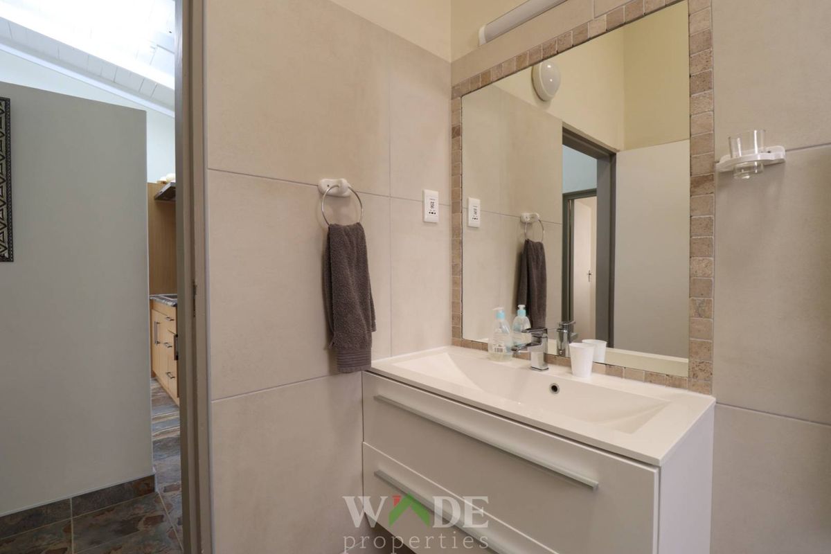 A modern bathroom featuring a wall-mounted vanity with an integrated basin, large mirror, and neutral wall tiling.