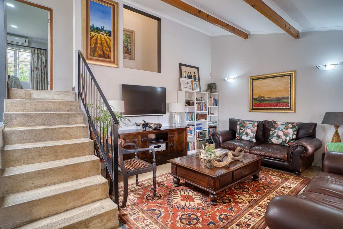 A cozy living room featuring exposed timber ceiling beams, a concrete staircase with a metal railing, and an open-plan layout.