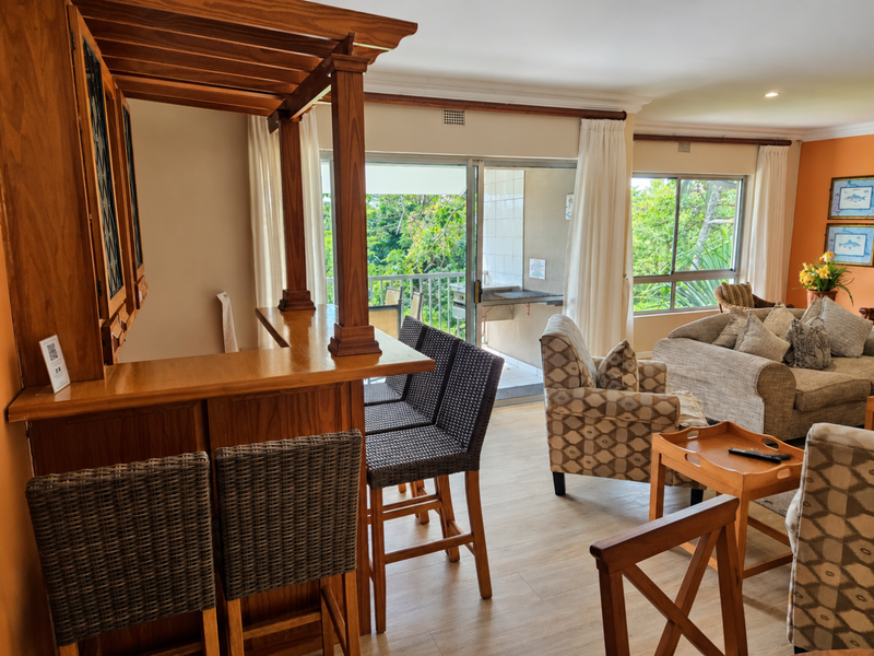 Open plan living area featuring a built-in wooden bar, laminate flooring, and sliding doors leading to a balcony with natural light.