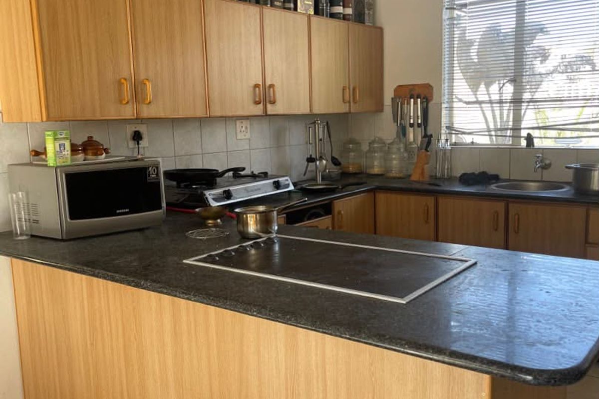 A functional kitchen featuring light wood-tone cabinetry, dark laminate countertops, a built-in hob, and tiled flooring with ample storage space.
