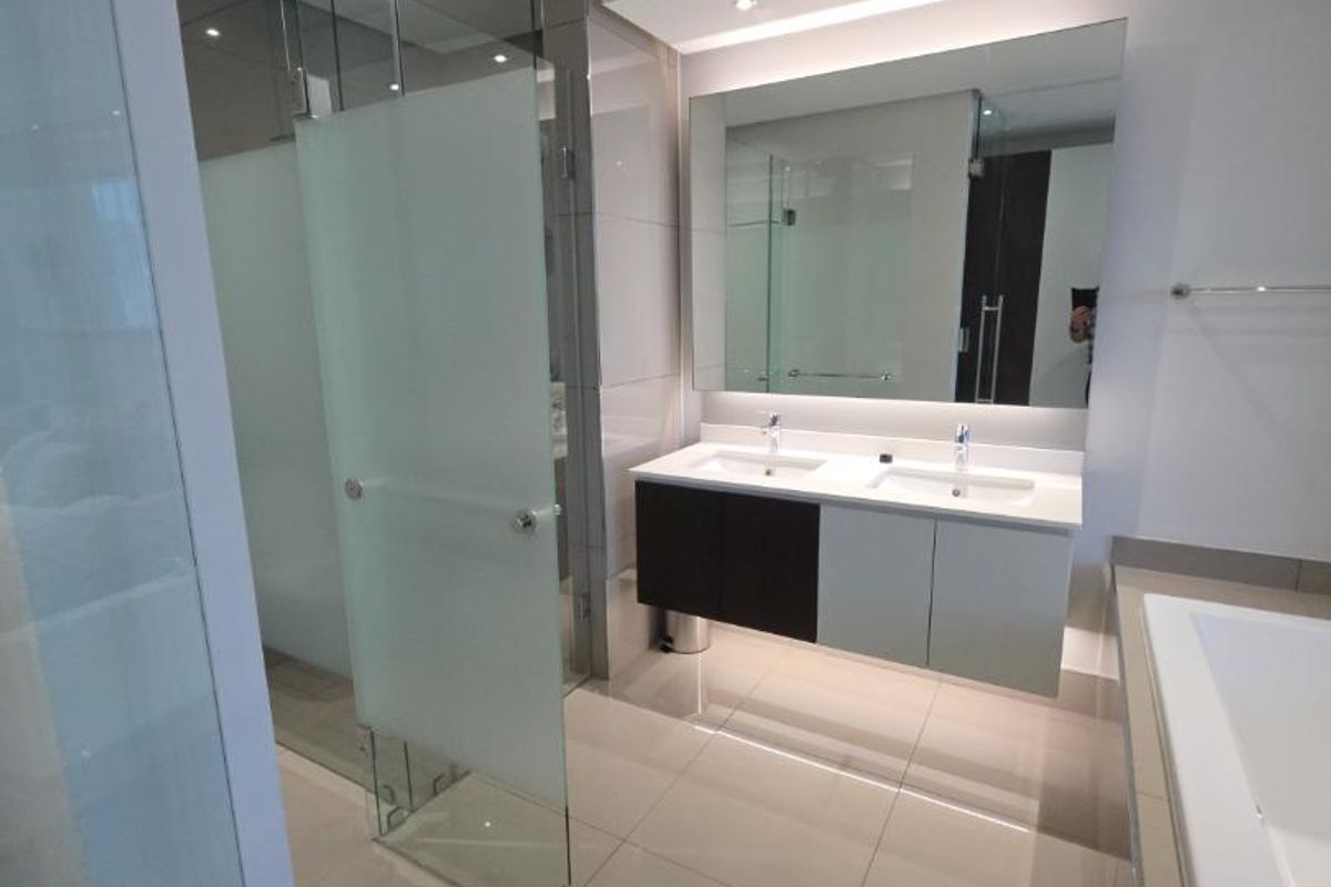 Modern bathroom featuring a double vanity with wall-mounted cabinetry, a large mirror, glass shower enclosure, and a built-in bathtub with neutral floor tiling.