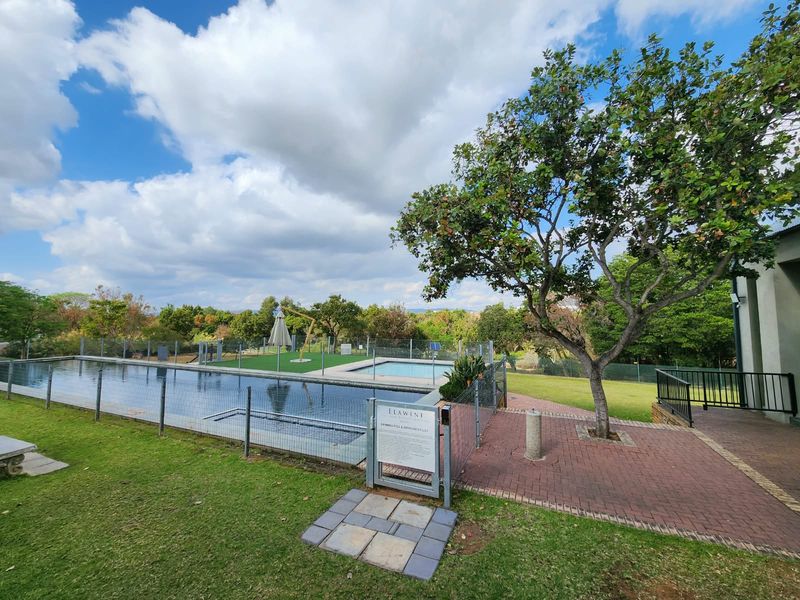 A well-maintained communal swimming pool area featuring paved walkways, perimeter fencing, and established landscaping within a residential estate.