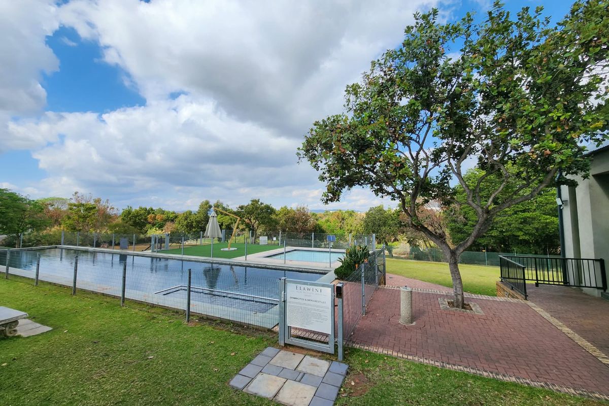 A well-maintained communal swimming pool area featuring paved walkways, perimeter fencing, and established landscaping within a residential estate.