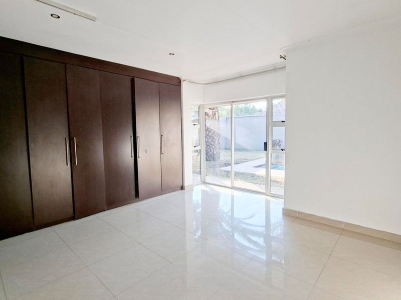 Spacious bedroom featuring large built-in cupboards, sleek tiled flooring, and a sliding glass door providing direct access to the garden and pool area.