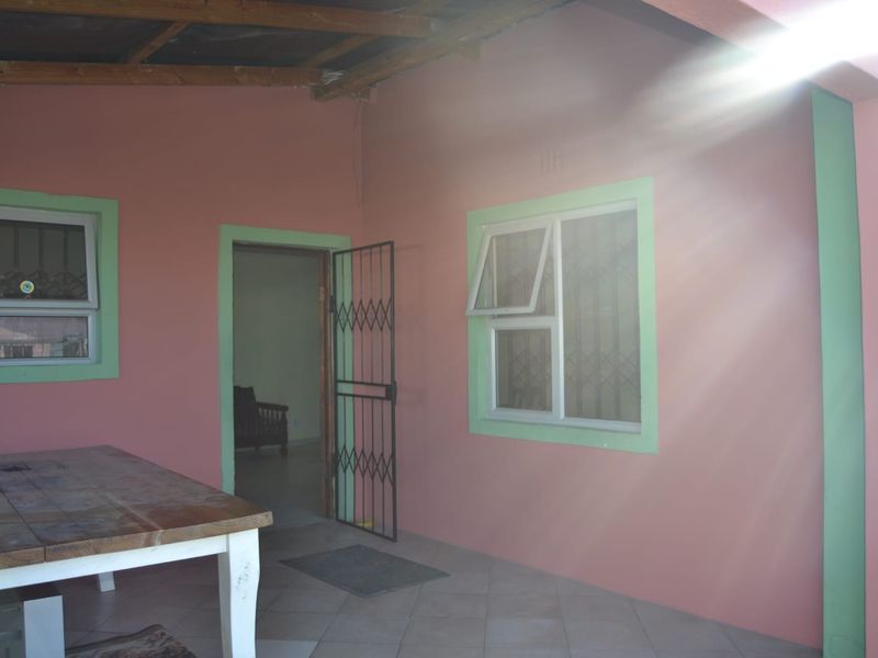 A covered patio area featuring tiled flooring, security gate access, and exposed timber rafters, offering a functional outdoor space for relaxation.