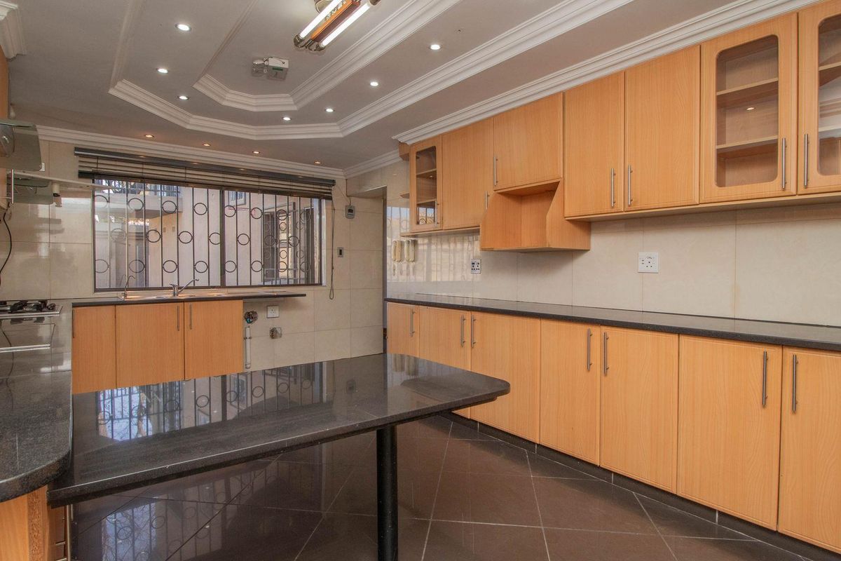 A spacious kitchen featuring light wood cabinetry, dark granite countertops, tiled flooring, and a recessed ceiling with integrated downlighting.