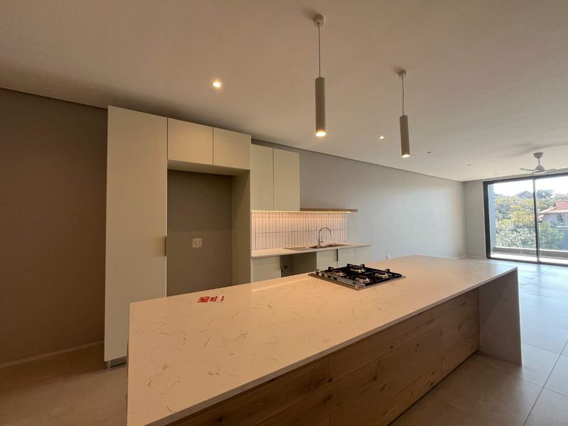 Modern open-plan kitchen featuring a large island with a gas hob, stone countertops, sleek cabinetry, and direct access to a balcony area.