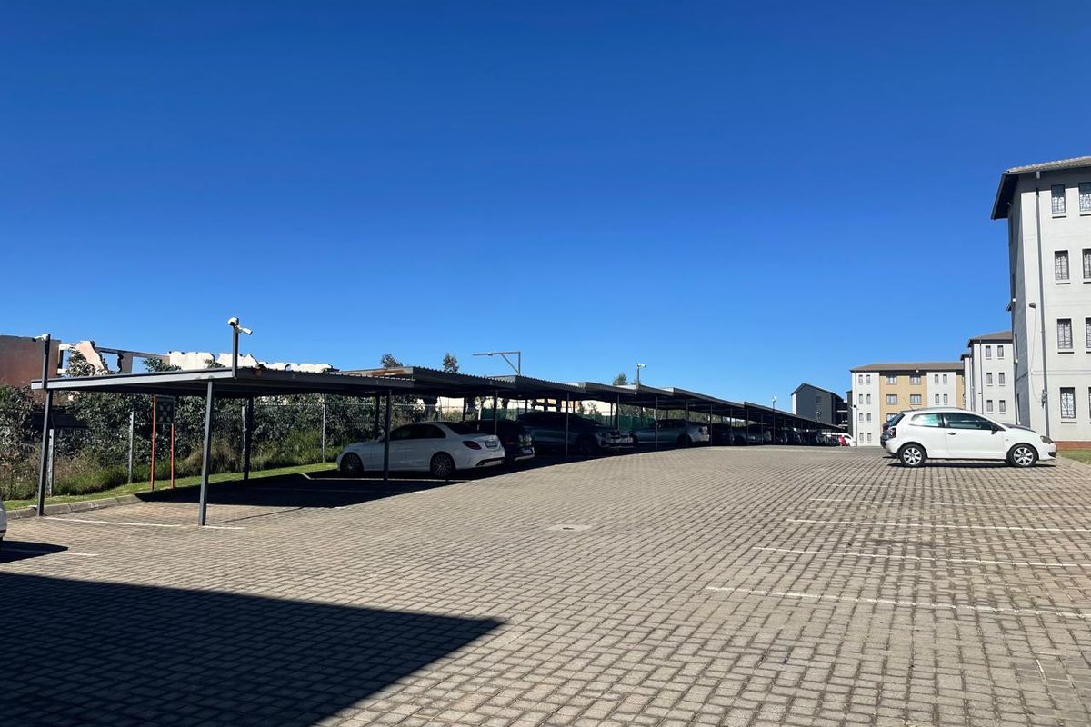 Outdoor parking area featuring covered carports with paved ground surfacing, situated adjacent to the apartment building complex.