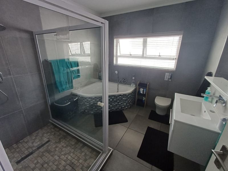 Modern bathroom featuring a corner bathtub, separate glass-enclosed shower, wall-mounted toilet, and a sleek vanity basin with contemporary grey wall tiling.