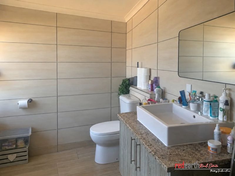 A modern bathroom featuring tiled walls, a granite-topped vanity with a vessel sink, and a wall-mounted toilet.