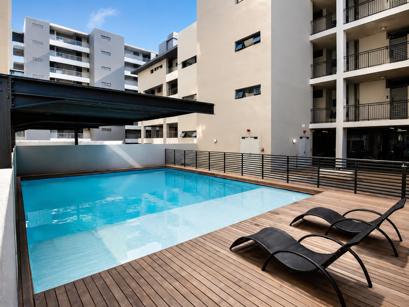 Modern apartment complex pool area featuring a swimming pool, timber decking, and a steel pergola structure.