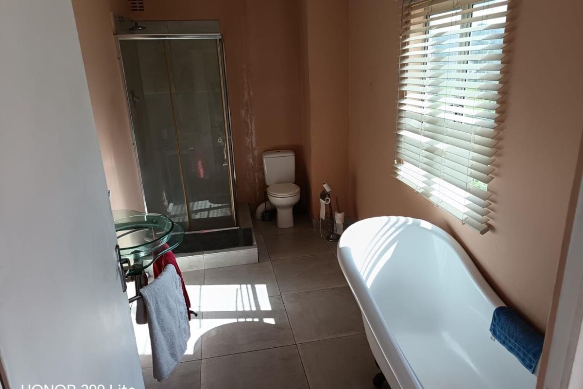 Bathroom featuring a freestanding bathtub, glass shower enclosure, and glass vessel sink, with visible wall staining requiring attention.