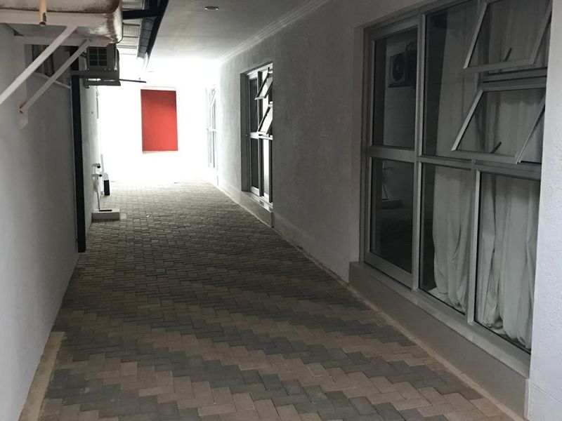 A paved exterior side walkway featuring aluminium window frames and an installed air conditioning unit.
