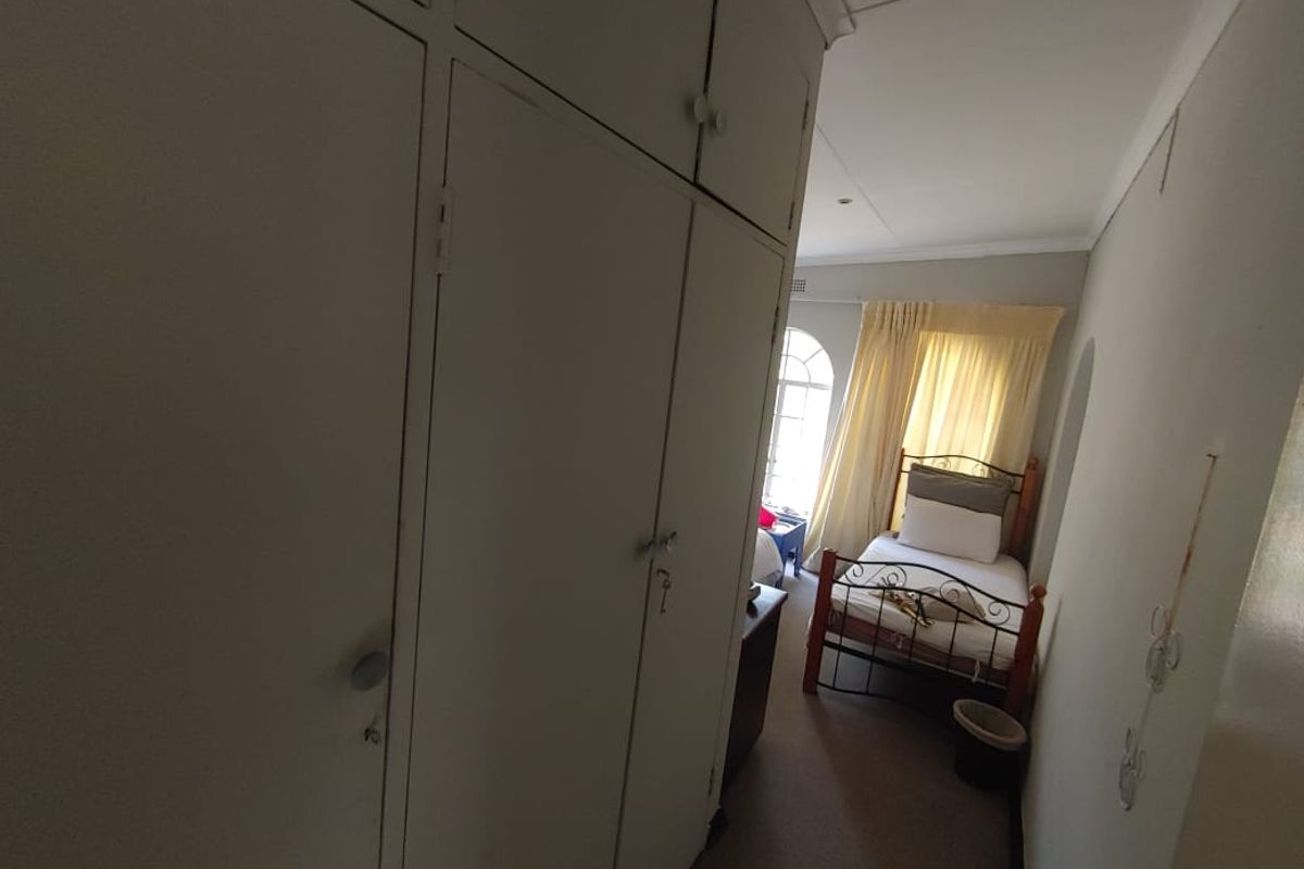 A bedroom featuring built-in cupboards and an arched window, requiring cosmetic updates to improve the overall condition of the wall finishes.