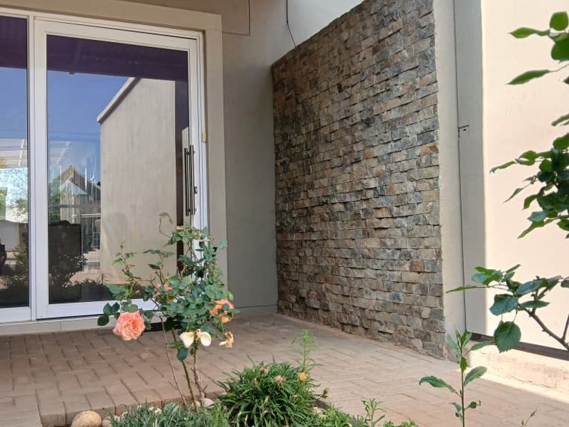 A covered patio area featuring a stone-clad feature wall, paved flooring, and a sliding glass door entrance.